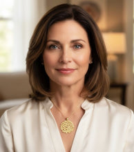 Woman wearing a white blouse and gold necklace in a softly blurred indoor setting