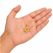 Gold Star of David pendant held in a hand on a white background