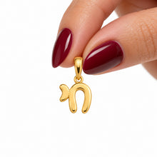 Delicate gold Chai pendant held between woman's fingers with burgundy nails, polished Hebrew symbol of life jewelry in 14K yellow gold