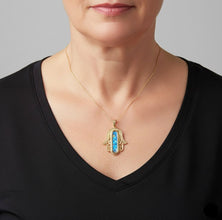 Woman wearing a black top with a gold necklace featuring a blue pendant.