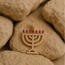 Gold menorah pendant with red gemstones on a stone surface