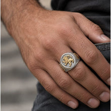 Hand wearing a silver and gold ring with a lion emblem on a blurred background