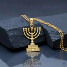 Gold Menorah pendant on a chain against a dark background