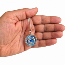 A silver-toned pendant necklace with a Star of David design and blue inlay, held in the palm of a hand against a white background.