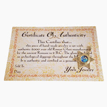 A Certificate of Authenticity card from Yoels Jewelry with ornate gold and beige scrollwork, featuring a gold star seal with a blue and green gemstone, on a plain white background.