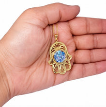 roman glass filigree hamsa pendant , held in the palm of a hand against a white background.