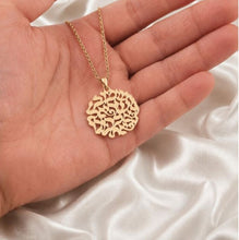 Gold necklace with a intricate pendant held in a hand on a white fabric background