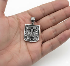 Silver pendant with Menorah design held in a hand against a white background