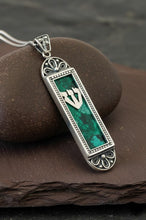 Silver Mezuzah pendant with green case on a dark stone surface