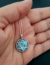 Star of David pendant held in a hand against a dark background