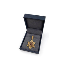 Gold star-shaped pendant with a red gemstone in a black box on a white background