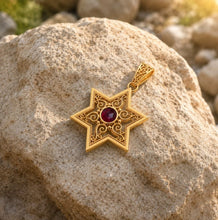 Gold star-shaped pendant with a red gemstone on a rock