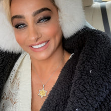 Woman wearing a black fur-lined coat with a star-shaped pendant in a car.