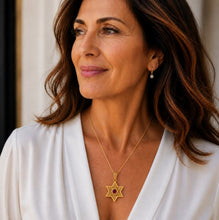 Woman wearing a gold necklace with a star pendant and a white top.