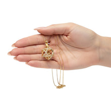 Hand holding a gold necklace with a decorative pendant on a white background